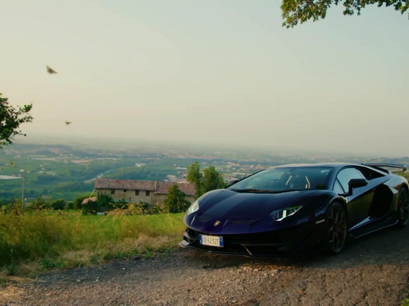 A Lamborghini parked on a hillside overlooking a valley at golden hour